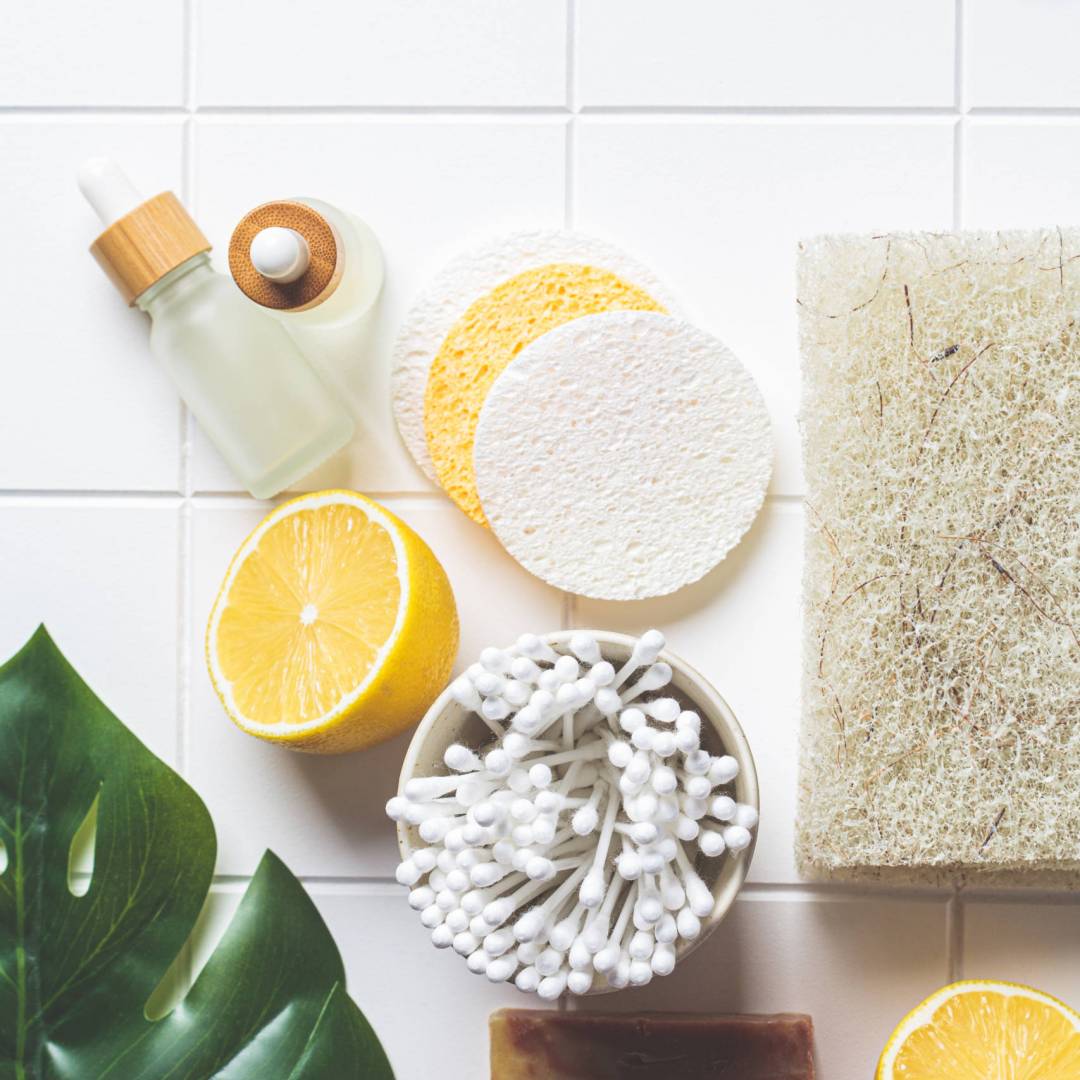 Eco bath accessories. Natural brushes, soap, sponges, organic skin care products and green leaves. White bathroom background, top view. Zero waste concept.